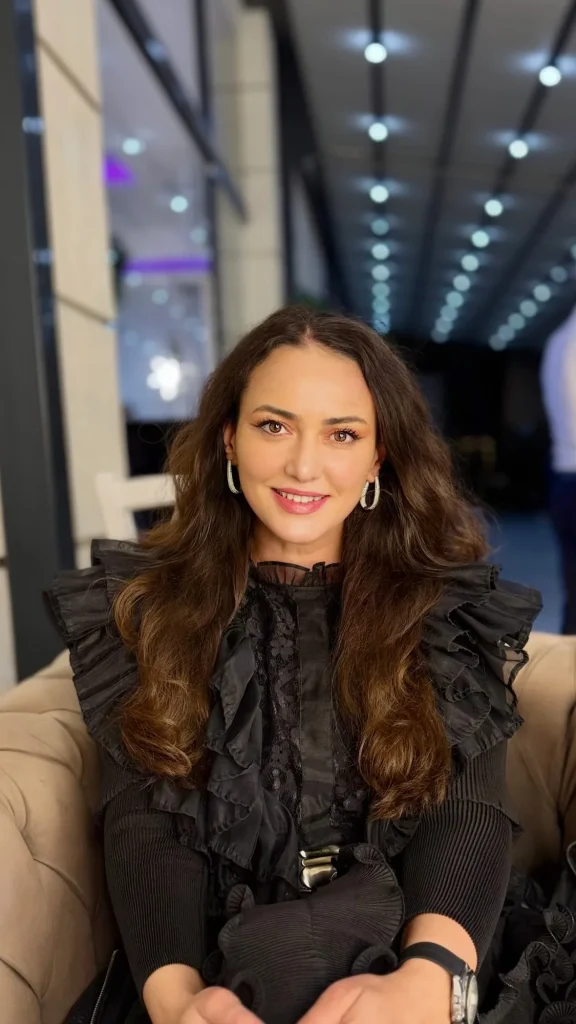 Ioana Balan zâmbind, așezată, în rochie neagră cu volane