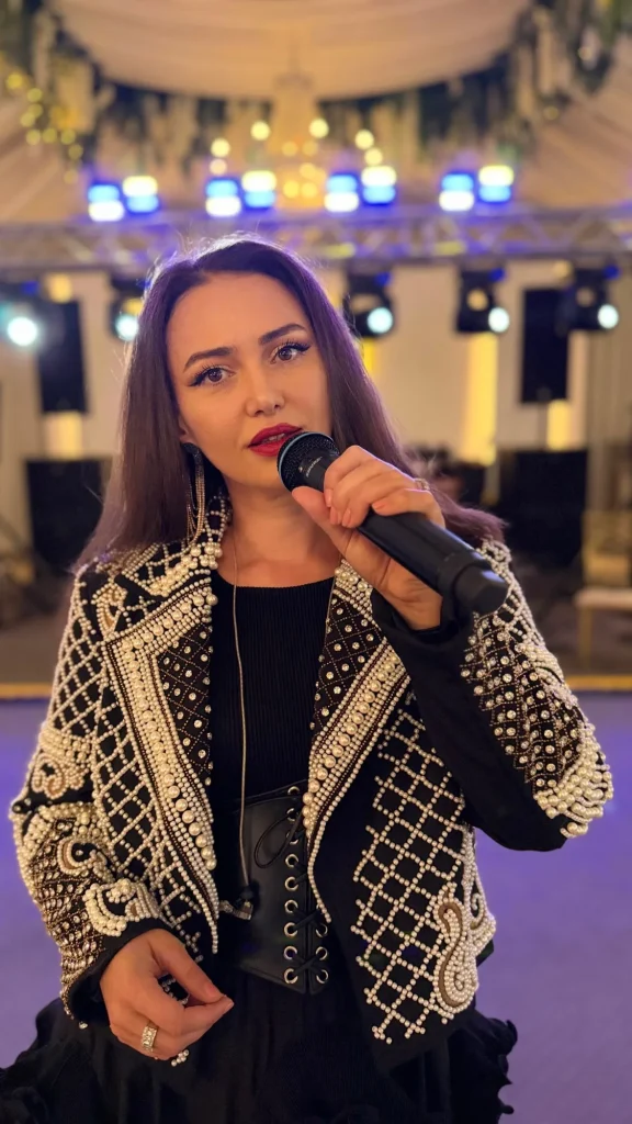 Ioana Balan cântând la microfon, în jachetă neagră brodată cu perle