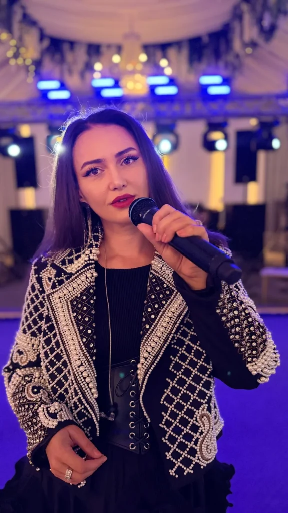 Ioana Balan cu microfonul, în jachetă cu perle, în lumina scenei