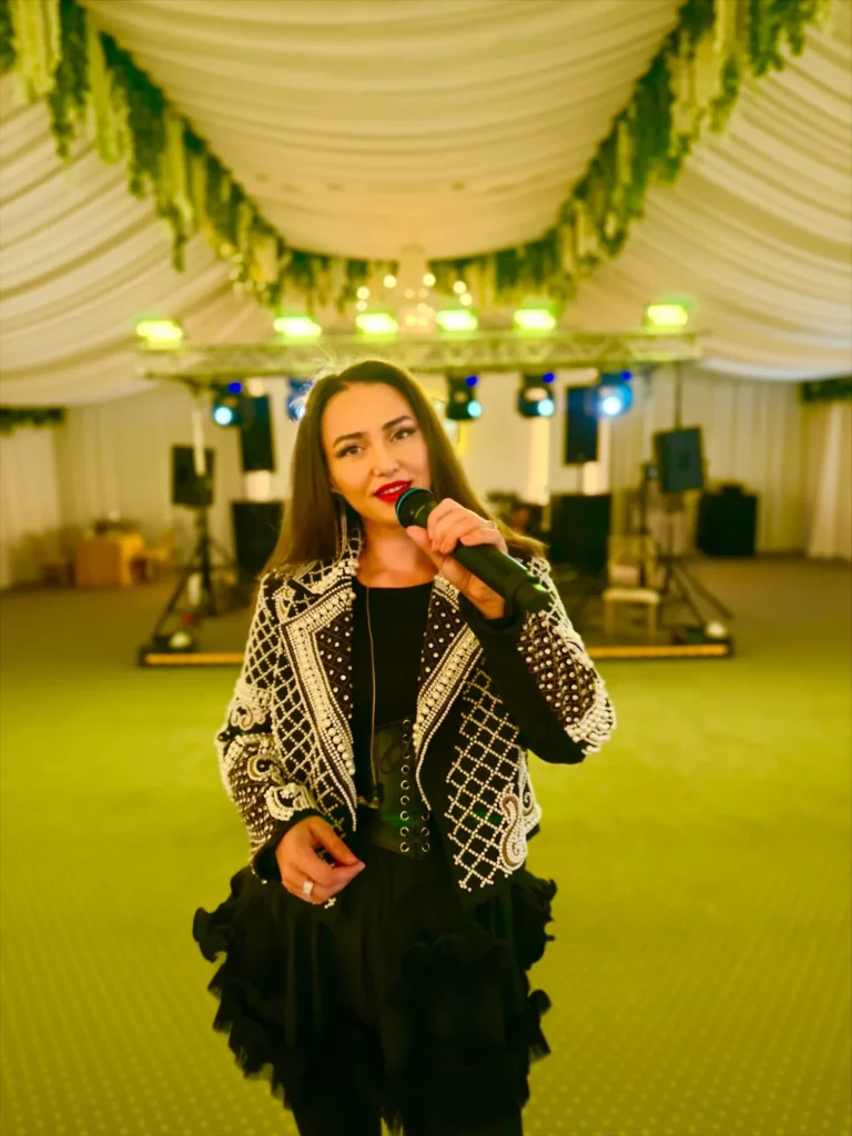Ioana Balan cu microfonul, în jachetă cu perle, într-un cort de evenimente