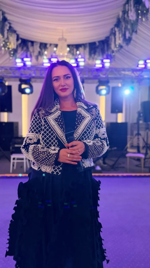 Ioana Balan în fața scenei, în jachetă cu perle și fustă neagră