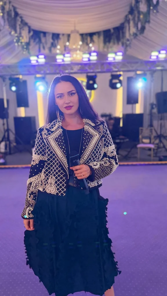 Ioana Balan în jachetă cu perle, în fața scenei, lumină mov