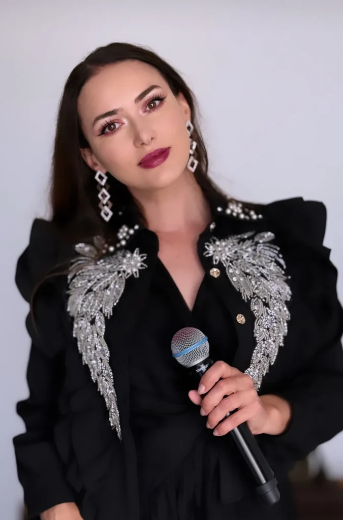 Ioana Balan cu microfonul, în sacou negru cu broderie argintie